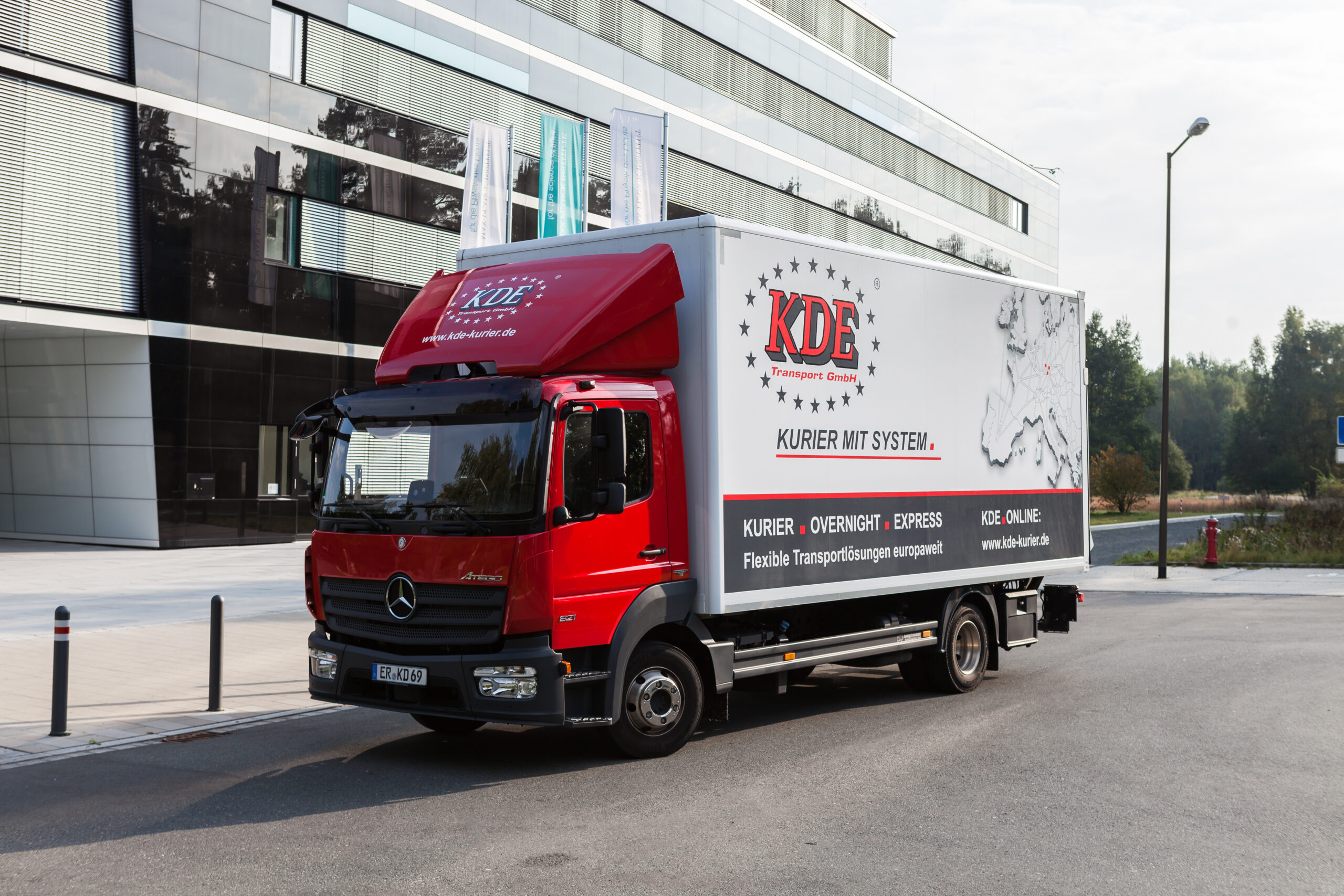 Ein neuwertiger LKW der KDE Transport GmbH steht vor einem Siemens-Gebäude und wartet auf seine Kurierfahrt.