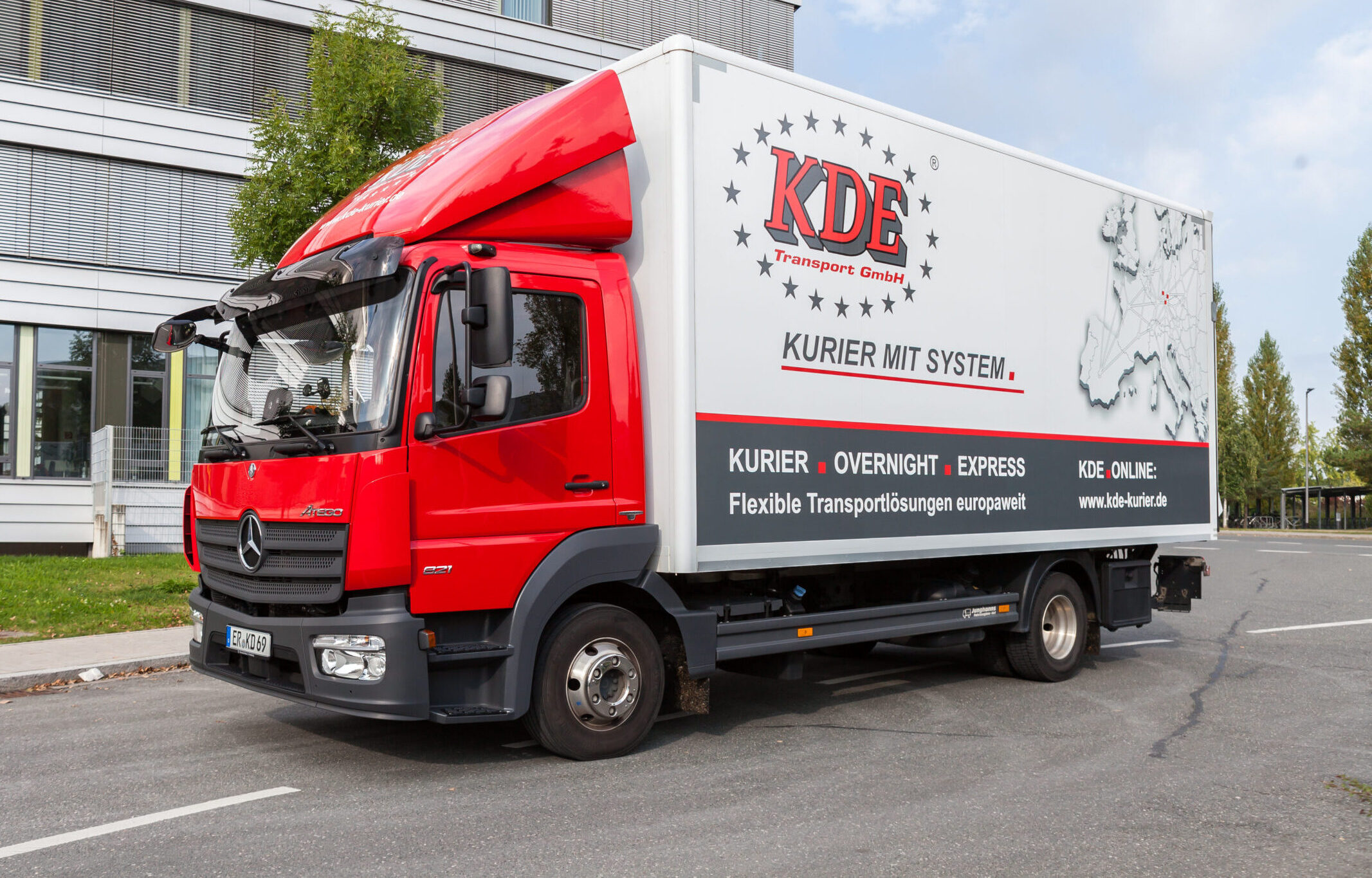 Das Foto zeigt einen modernen LKW der KDE Transport GmbH vor einem Firmengebäude.