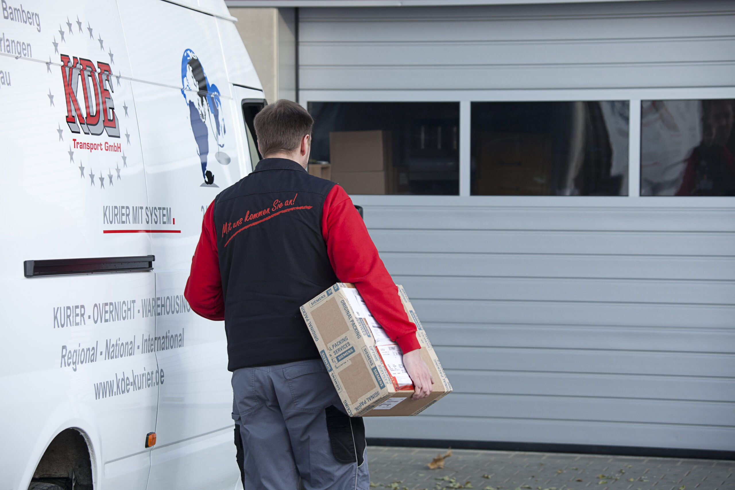 Ein Kurier der KDE Transport GmbH liefert ein Paket bei einem Kunden aus.