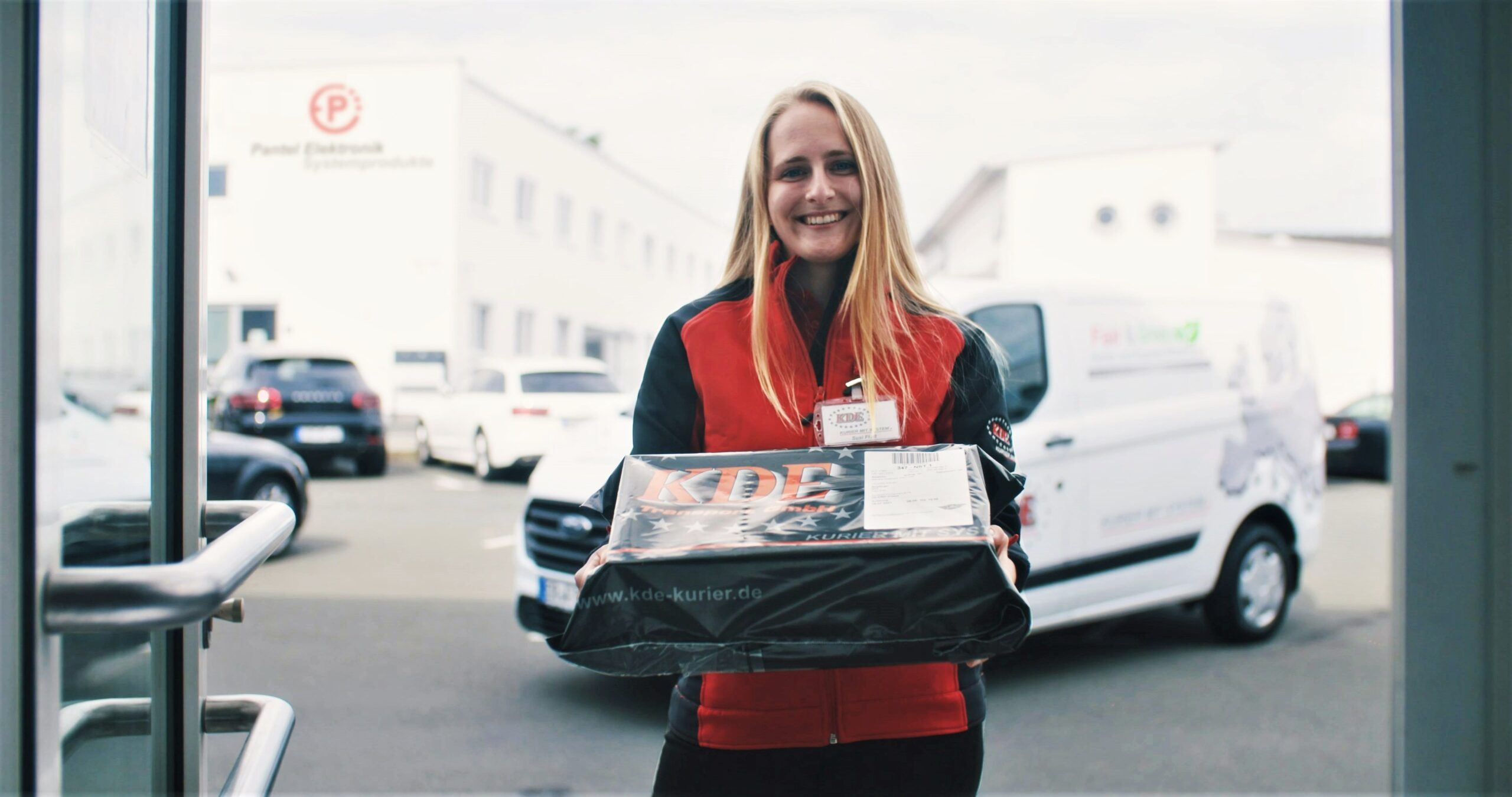 Eine Kurierin der KDE Transport GmbH übergibt an der Eingangstür persönlich die Ware, die in einer dokumentensicheren KDE-Versandtasche verpackt ist.