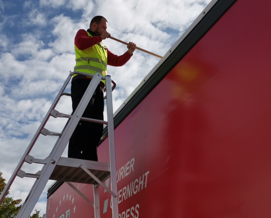 Ein Kurier befreit das Dach eines LKW von Schnee mit der Schneeleiter.