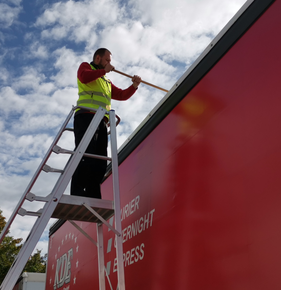 Ein Kurier befreit das Dach eines LKW von Schnee mit der Schneeleiter.